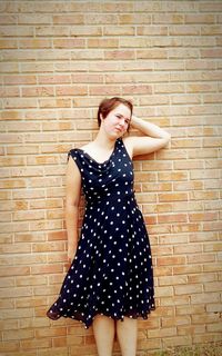 Portrait of young woman standing against brick wall