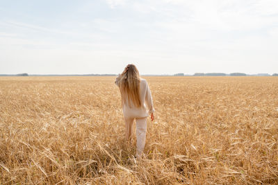 A woman is gracefully walking through a beautiful golden wheat field beneath a bright sky