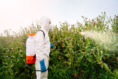 Side view of person in protective workwear spraying herbicide on field