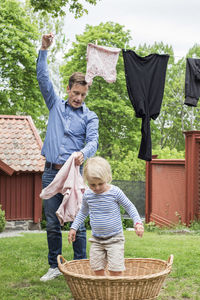 Girl standing in laundry basket while father removing clothes from clothesline