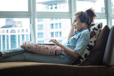 Side view of woman sitting on window at home