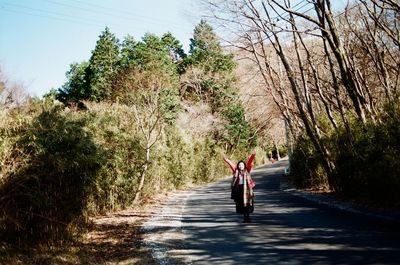 Woman on road amidst trees against sky