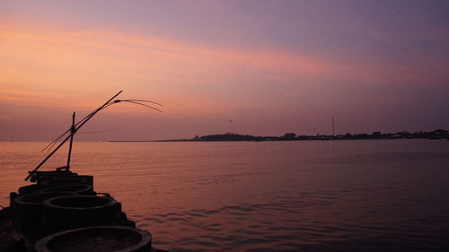 Fishing rod on sea against sky during sunset