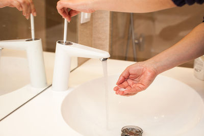 Cropped image of person washing hands at sink in bathroom
