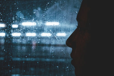Close-up of silhouette woman looking through window at night during rainy season