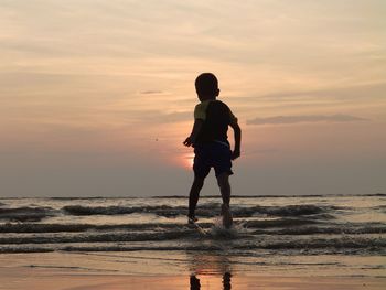 Full length of boy standing on beach against sky during sunset