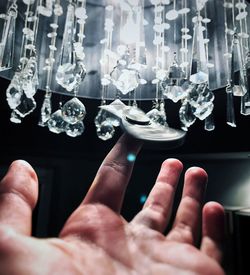 Cropped hand touching illuminated chandelier at home