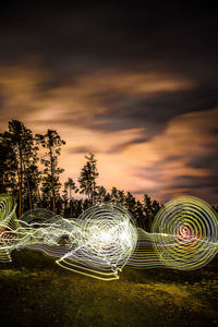Light trails on illuminated tree against sky at night