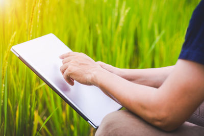 Midsection of man holding laptop while sitting against plants