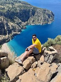 Young man sitting on rock beside blue ocean at turkey 