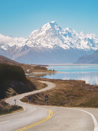 Road by lake against snowcapped mountains