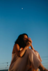 Low angle view of woman standing against clear blue sky