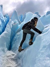 Portrait of woman climbing on glaciers against cloudy sky during winter