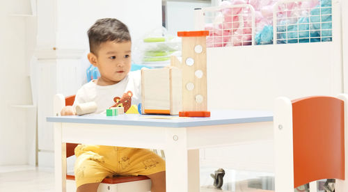 Cute boy playing with toys while sitting on table at home