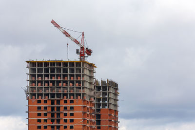 Low angle view of crane by building against sky