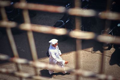 Man walking on road seen through metal grate