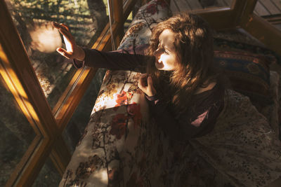 Young redhead woman sitting on sofa and looking through window