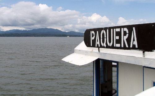 Information sign by sea against sky