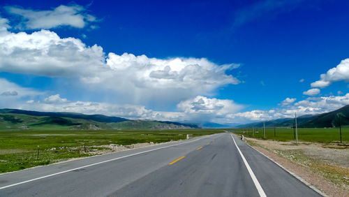 Empty road amidst landscape against blue sky