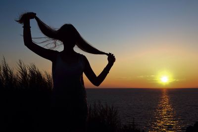 Silhouette woman holding her hair at beach against sky during sunset