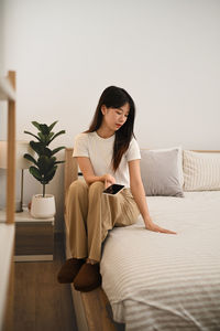 Young woman using mobile phone while lying on bed at home