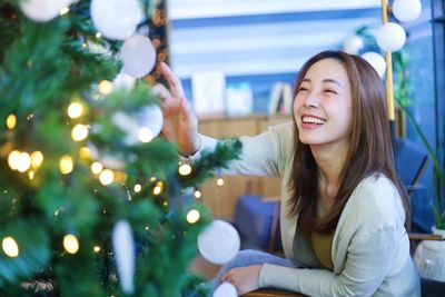 Portrait of young woman sitting on christmas tree at night