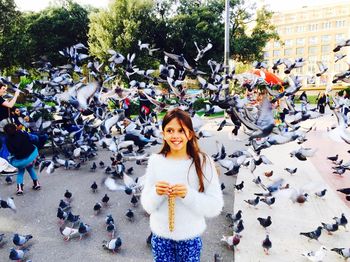 Smiling girl standing amidst flying pigeons