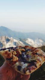 Close-up of hand holding pizza against mountain range