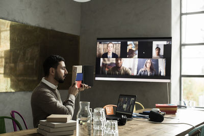 Male entrepreneur reading diary during meeting on video conference in creative office