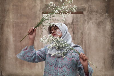 Close-up of muslim woman holding flowers while standing against wall