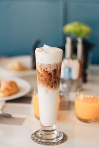 Iced cappuccino coffee in a tall glass cup on table with breakfast background. 