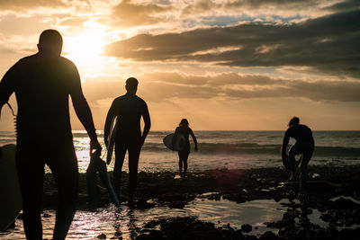 Silhouette people on beach against sky during sunset