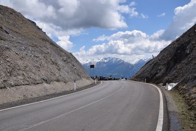 Empty road leading towards mountains against cloudy sky