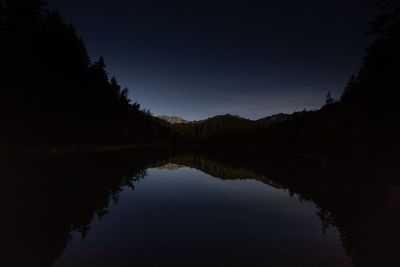 Reflection of silhouette trees in lake against sky at night