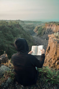 The man on the edge of the cliff was relaxing and reading a book. kaliadem, yogyakarta