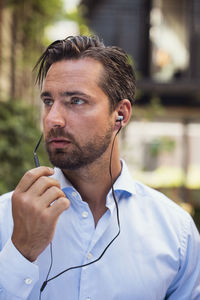 Confident businessman talking through in-ear headphones at office yard