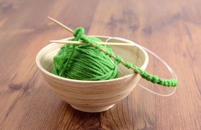 Knitting needles with ball of green wool on table