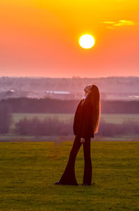 Woman standing on field against sky during sunset