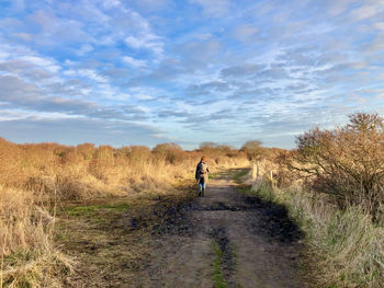 Rear view of woman walking on field against sky