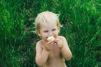 Shirtless cute girl eating food while sitting on grassy field
