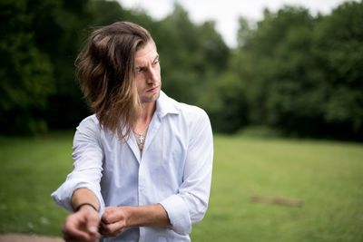 Man folding sleeve while standing on field against trees