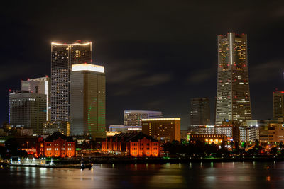 Illuminated buildings by river against sky at night