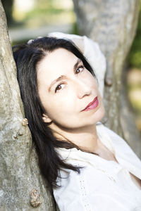 Portrait of smiling young woman against tree trunk