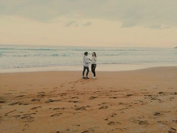 Rear view of friends on beach against sky during sunset