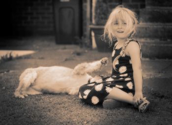 Full length of girl looking away while sitting by dog on field