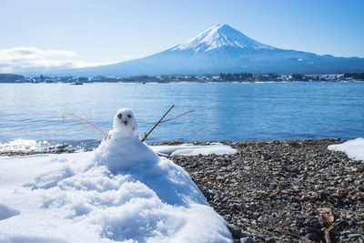 Snowman at lakeshore against snowcapped mountain
