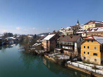 Houses by river in town against clear sky