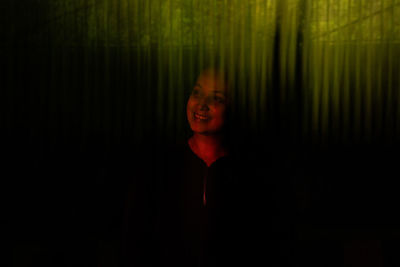 Portrait of smiling young woman standing against black background