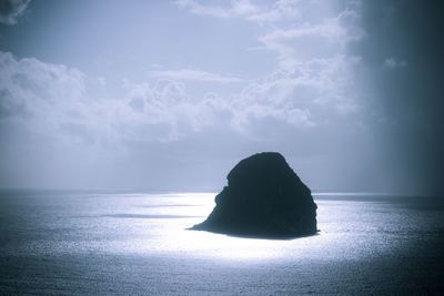 Silhouette rock in sea against sky