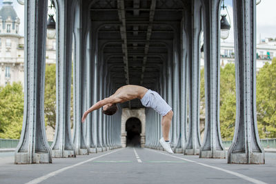 Side view full length of shirtless man jumping below bridge